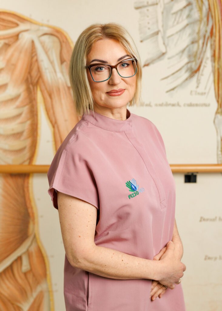 Kobieta w okularach stoi przed ścianą z rysunkami antomicznymi.