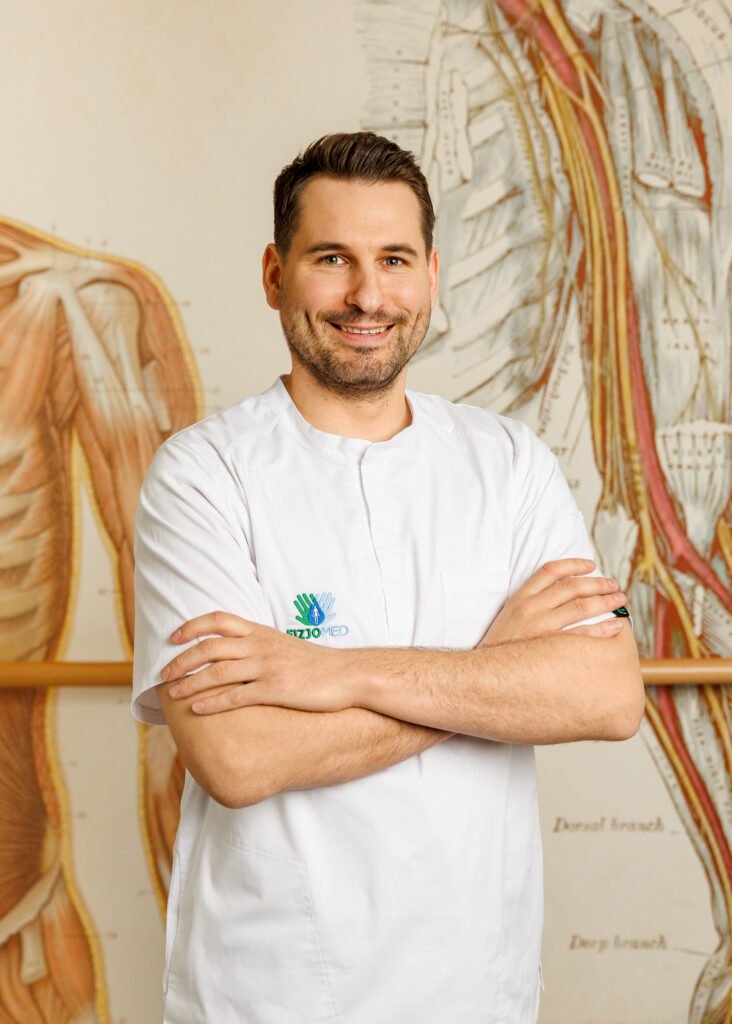 Uśmiechnięty mężczyzna soi przed ścianą z ilustarcjami anatomicznymi.