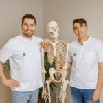 Dwóch fizjoterapeutów pozuje z modelem ludzkiego szkieletu