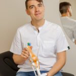 Fizjoterapeuta w kitlu siedzi na leżance, trzymając model kolana