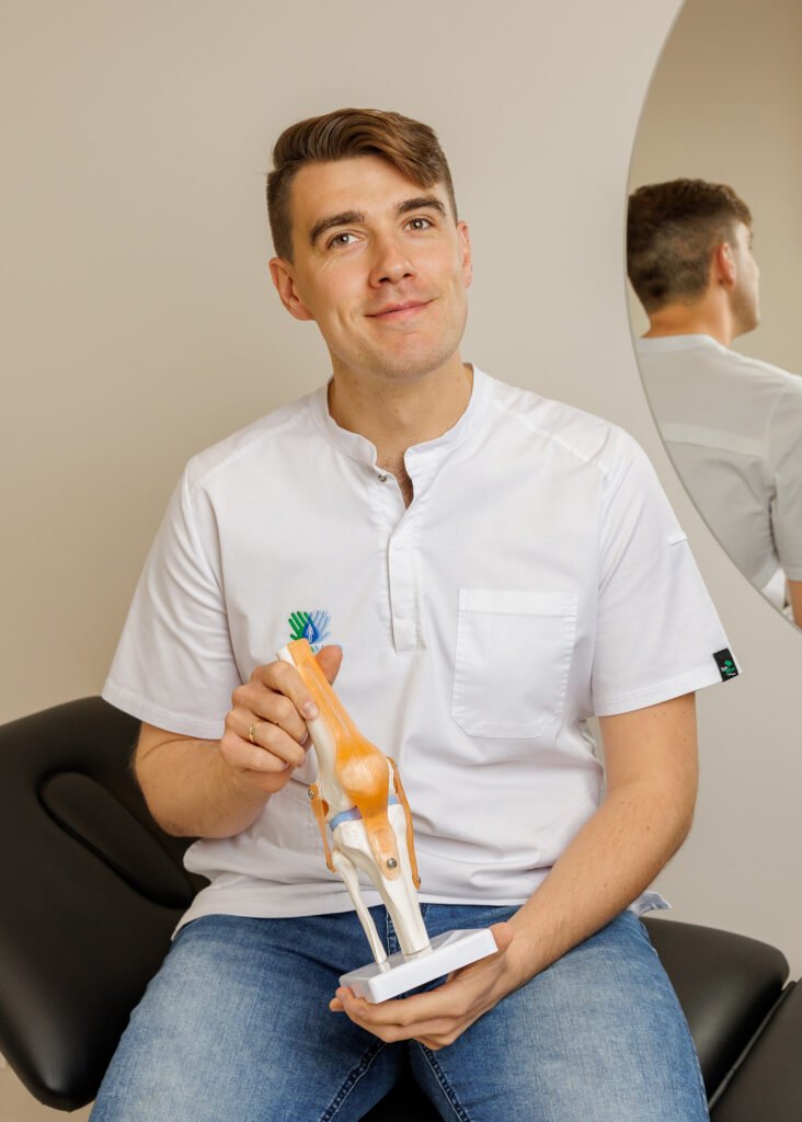 Fizjoterapeuta w kitlu siedzi na leżance, trzymając model kolana